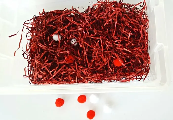 Red tinsel and pompoms for a toddler sensory bin activity