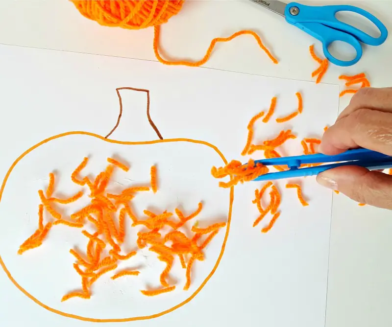 Sprinkle yarn pieces over pumpkin cut out with tongs