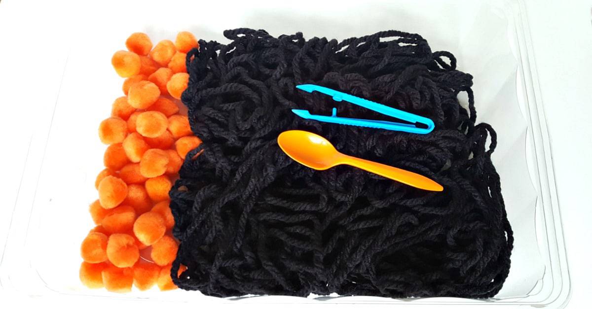 Yarn and pompoms in the sensory bin for a toddler Halloween fine motor activity